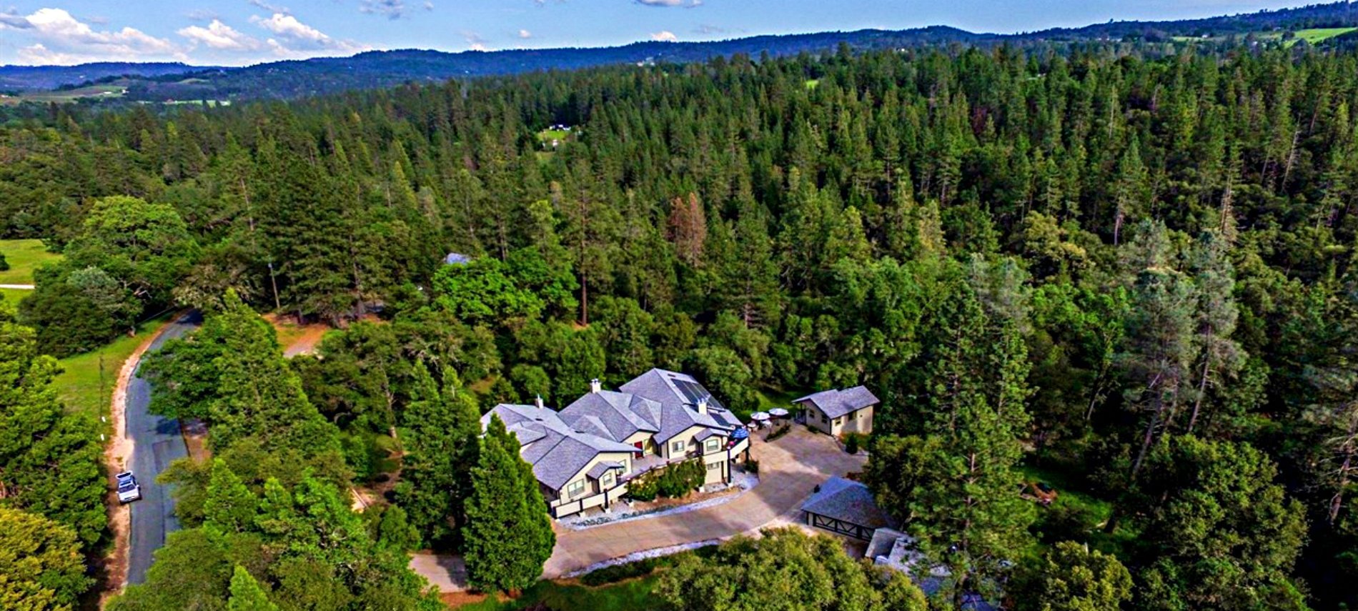 A aerial view of the Inn as is sits on a sloped driveway amidst a lush, green forest. 